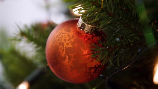 Handheld, shallow depth of field close up of glittering baubles hanging on a Christmas tree with fairy lights - 映像、動画