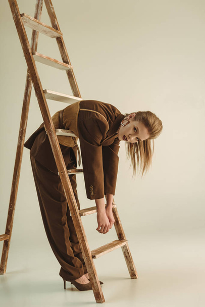 attractive young woman in vintage style posing near wooden ladder on beige - Fotoğraf, Görsel