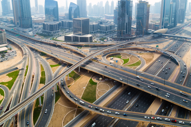 Εναέρια άποψη του Ντουμπάι γέφυρα στον ορίζοντα της πόλης κυκλοφορία στον αυτοκινητόδρομο. Μεταφορά οδική κυκλοφορία ΗΑΕ με εναέρια άποψη κυκλοφορίας οχήματος. Το top view. Γραφική οδό φόντο. - Φωτογραφία, εικόνα