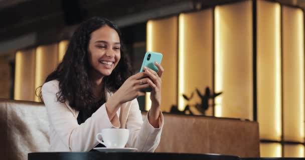 Business woman using smartphone in cafe drinking coffee laughing in cafe. Communication, successful business, dating, good mood concept - Materiaali, video