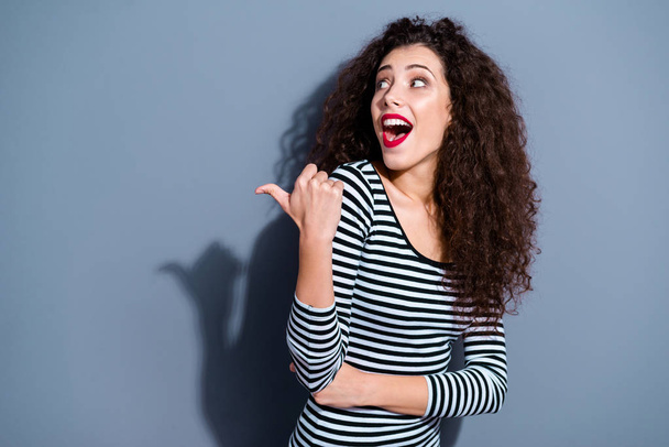 Portrait of her she nice cute charming winsome attractive lovely cheerful cheery amazed wavy-haired lady pointing thumb aside ad opened mouth isolated over gray pastel background - Foto, imagen