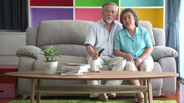 Старший пара сидить і дивиться телевізор у вітальні. Відставний старі азіатських чоловіки і жінки, відпочити у вітальні-диван, щасливою усмішкою. Концепція старших способу життя. - Кадри, відео