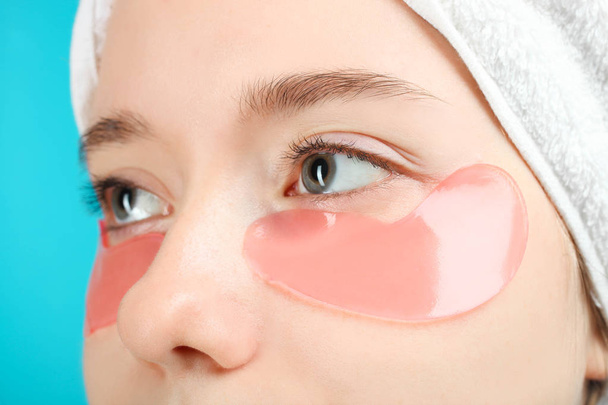 Female face with pink eye patches on blue background. Concept self care. Clothe-up. - Foto, imagen
