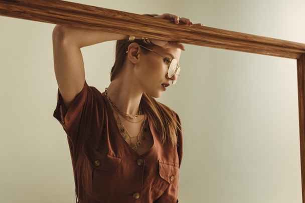 beautiful stylish girl posing with big wooden frame isolated on beige - Φωτογραφία, εικόνα