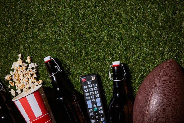 flat lay of brown bottles near popcorn, remote control and ball lying on grass - Fotó, kép