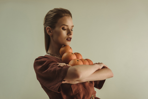 beautiful fashionable woman holding fresh oranges isolated on beige - Foto, Imagen