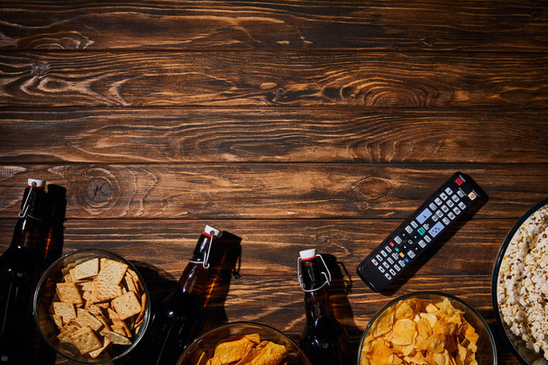 top view of tasty snacks near bottles and remore controll on wooden table - Fotoğraf, Görsel