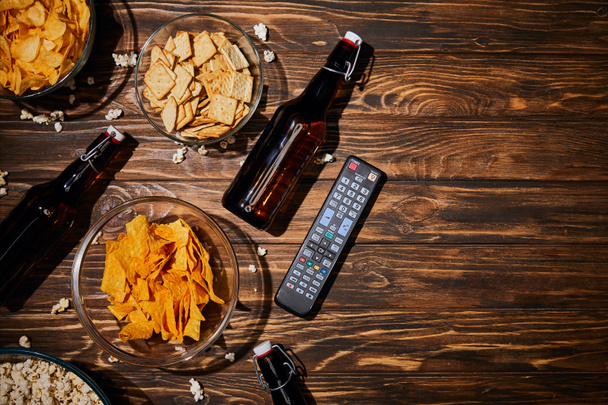 pohled shora občerstvení u lahve s pivem a dálkové ovládání na dřevěný stůl - Fotografie, Obrázek