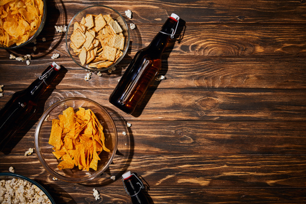 top view of snacks in bowls near brown bottles with beer on wooden table - Photo, Image