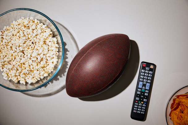 top view of delicious snacks in glass bowls near football and remote control on white background - Photo, Image
