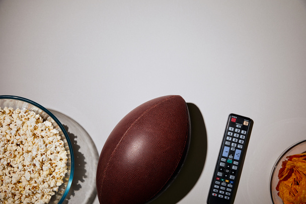 bovenaanzicht van popcorn in kom in de buurt van de bal en afstandsbediening op witte achtergrond - Foto, afbeelding