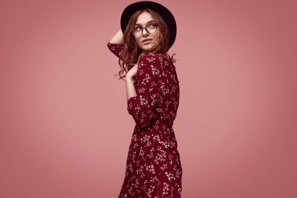 Portret zmysłowy elegancki blask hipster dziewczyna moda czerwona sukienka, czarny kapelusz i okulary pozowanie na kolorowy różowy tło w studio - Zdjęcie, obraz