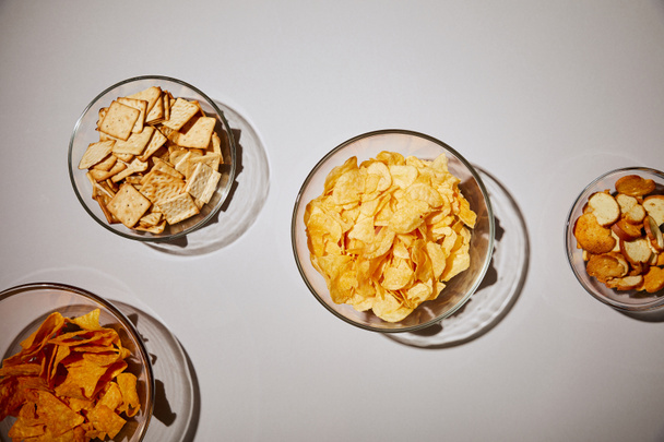 top view of glass bowls with tasty snacks on white background - Zdjęcie, obraz