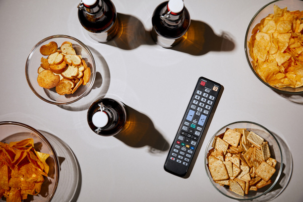 top view of bottles with beer near remote control and snacks in bowls on white background - Photo, image