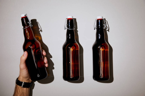vista recortada del hombre sosteniendo la botella con cerveza sobre fondo blanco
 - Foto, Imagen