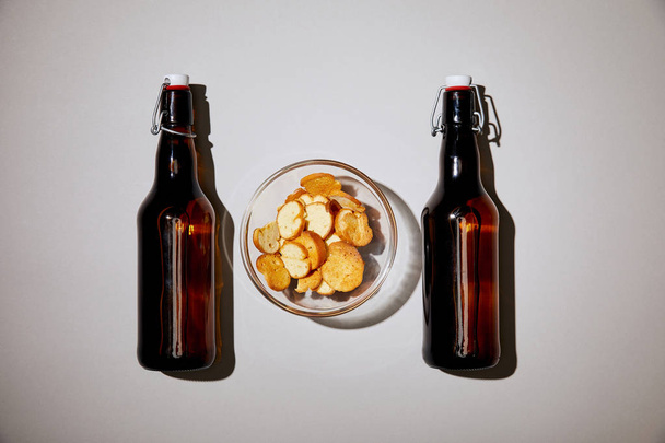 top view of brown bottles with beer near snack in bowl on white background - Foto, imagen
