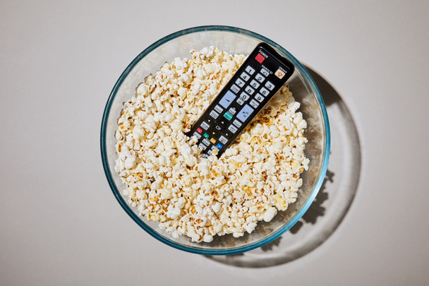 top view of tasty popcorn in bowl with remote control on white background - Fotó, kép