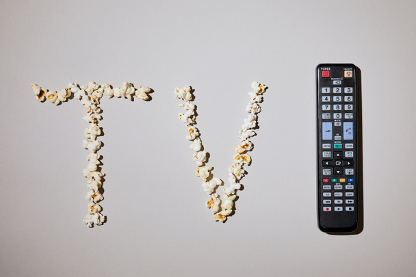 top view of tasty popcorn with tv lettering with remote control on white background - Photo, Image