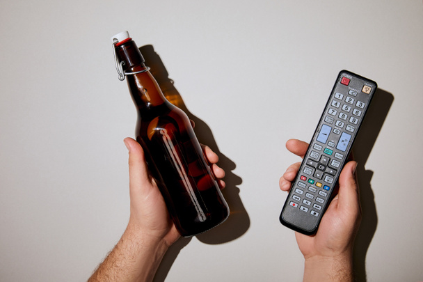 περικοπεί θεώρηση του ανθρώπου που κρατώντας το μπουκάλι μπύρας με απομακρυσμένο έλεγχο στα χέρια σε λευκό φόντο - Φωτογραφία, εικόνα