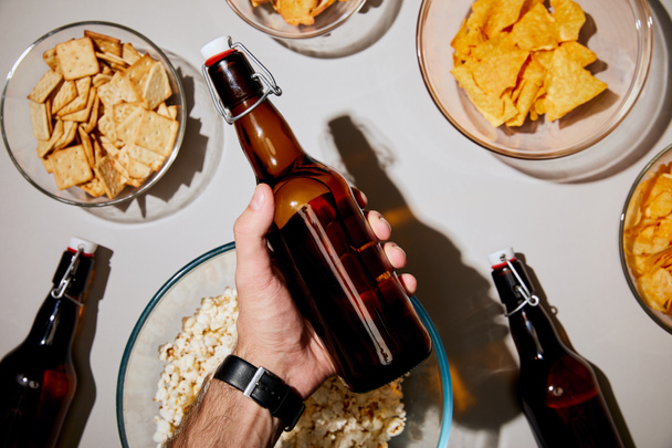 selective focus of man holding bottle with beer near snacks in bowls on white background - Foto, immagini