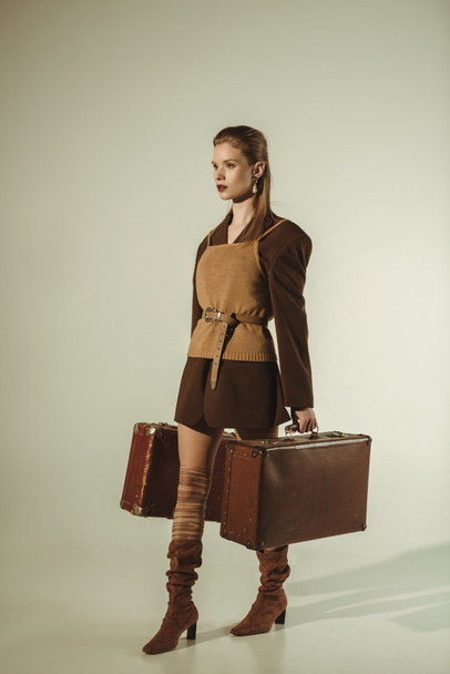 attractive young woman holding vintage travel bags on beige - Фото, зображення