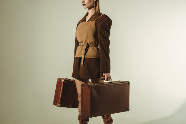 cropped view of stylish woman holding retro travel bags on beige - Foto, Imagem