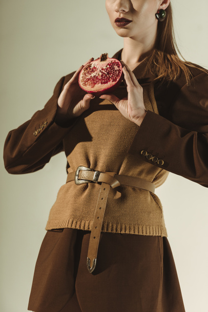 vista recortada de la mujer con estilo que sostiene la mitad de la granada fresca aislada en beige
 - Foto, imagen