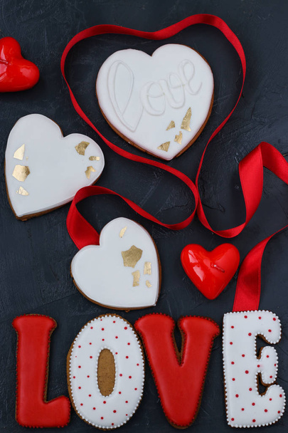Homemade gingerbreads in the shape of hearts and the letters "love" for Valentine's Day are located on a dark background, top view - Фото, изображение