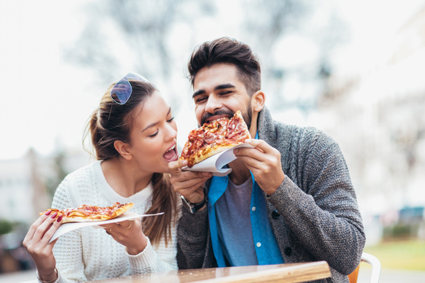 Pareja comiendo pizza al aire libre y sonriendo.Están compartiendo pizza en un café al aire libre. - Foto, Imagen