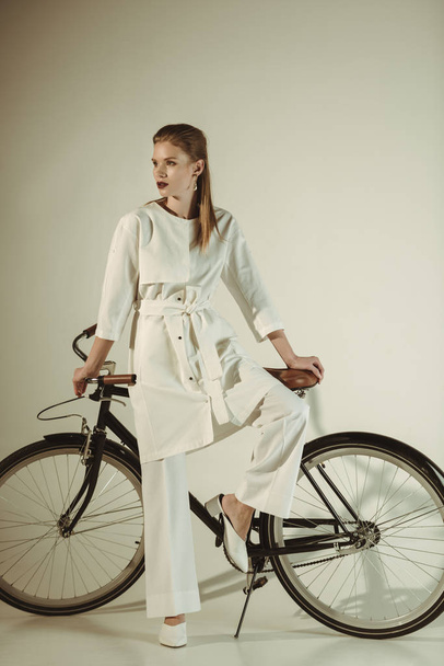 attractive stylish girl in white outfit posing on bicycle - Фото, зображення