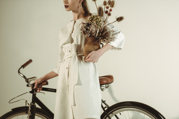 cropped view of stylish woman posing with bouquet of dry flowers near bicycle - Foto, Bild