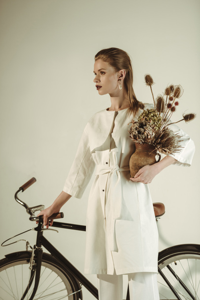 attractive stylish girl posing with bouquet of dry flowers near bicycle - Foto, Bild