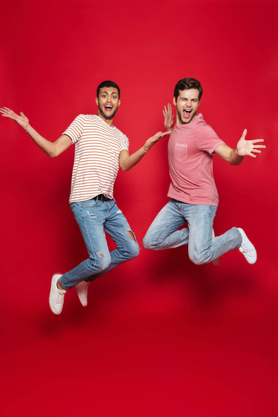 Two cheerful men friends jumping isolated over red background - Foto, Bild