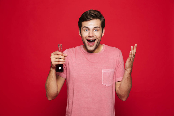 Image of a handsome happy young man posing isolated over red wall background drinking soda. - Zdjęcie, obraz
