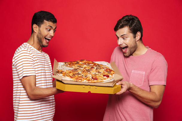 Image of a handsome happy young men friends isolated over red wall background holding big pizza. - Fotó, kép