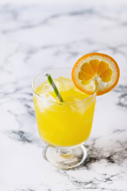 Νόστιμο χυμό πορτοκαλιού, σε ποτήρι με πάγο κύβος μπλε και το λευκό φόντο κάθετη φρέσκα πορτοκάλια - Φωτογραφία, εικόνα