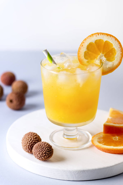 Smakelijke jus d'orange in glas met een Ice Cube blauw en wit achtergrond verse sinaasappelen verticaal - Foto, afbeelding