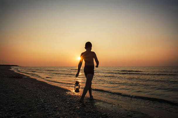 Young boy with lamp at sunrise on the beach - Foto, Bild