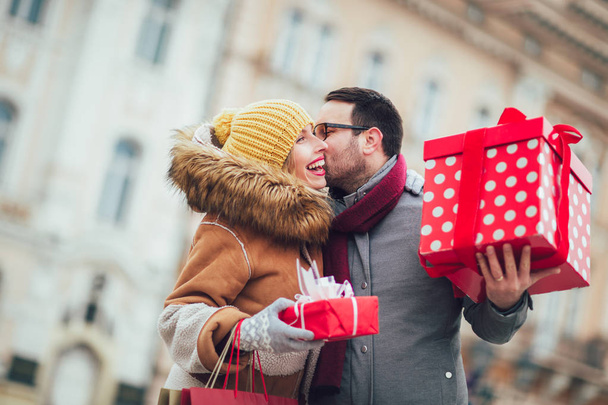 Jeune couple vêtu de vêtements d'hiver tenant des boîtes cadeaux en plein air
. - Photo, image