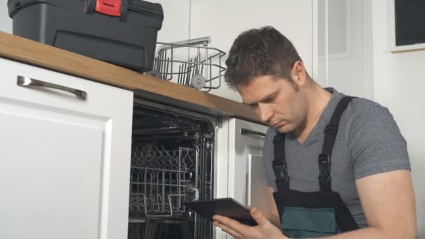 Handyman com tablet pc reparação de máquina de lavar louça doméstica na cozinha
. - Filmagem, Vídeo