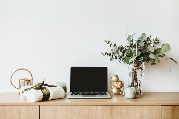 Blogger, freelance home office desk workspace. Laptop with mock up screen on wooden desktop decorated with eucalyptus bouquet, gift box, candles on white background. Blog, website, social media hero header. - Foto, Bild