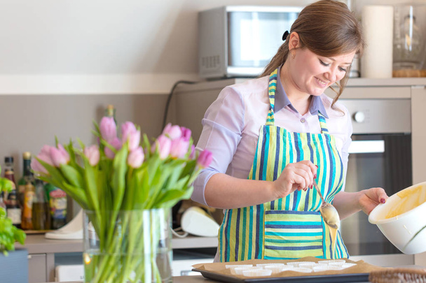  Beautiful young woman baking cupcakes at kitchen - Fotó, kép