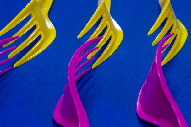 Padrão de garfos coloridos de plástico amarelo e roxo colocado no final formando uma onda sobre um fundo azul com espaço de cópia. Tendências de cor e conceito de problema de resíduos plásticos
 - Foto, Imagem