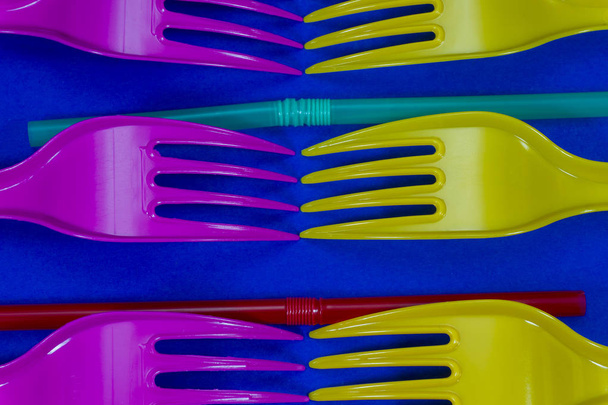 Желтые и розовые столовые приборы пластиковые вилки и соломинки расположены на синем фоне. Концепция цветовых тенденций и проблемы пластиковых отходов
 - Фото, изображение