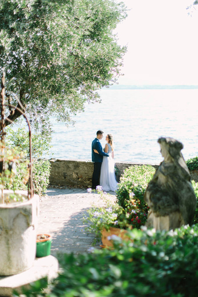 Beautiful young woman in blue dress and handsome man in suit walking in the garden of Rocca Scaligera medieval castle, Sirmione town, Garda lake, Italy - Фото, изображение