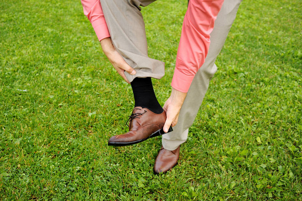 The man takes off his shoe, standing on the grass. Classic suit, black socks. - Zdjęcie, obraz