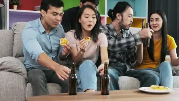 Group of friends eating pizza and drinking beer on sofa. Mixed race young people enjoying pizza and beer together, cheering and toasting action. House party concept.  - Imágenes, Vídeo