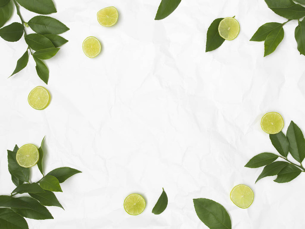 limes and green leaves on white crumpled background - Zdjęcie, obraz