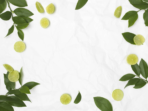 limes and green leaves on white crumpled background - Zdjęcie, obraz