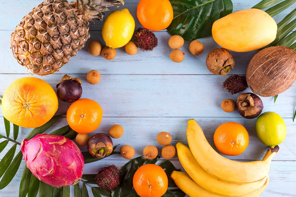 Здорові веселкові тропічні фрукти рамка з пальмовим листям на синьому дерев'яному столі, вид зверху, місце для тексту
 - Фото, зображення